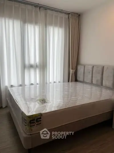 Spacious bedroom with large windows and elegant curtains, featuring a new mattress on a stylish bed frame.