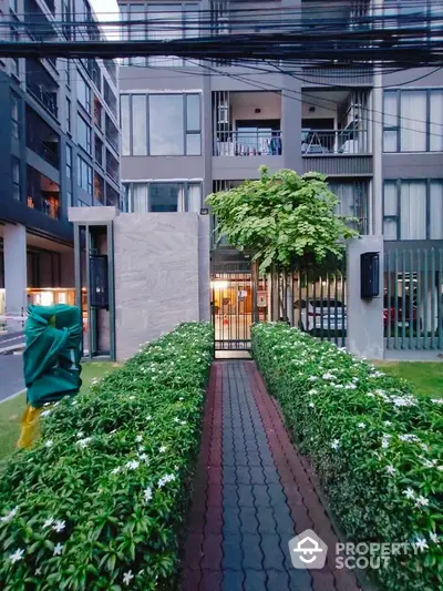 Modern apartment building entrance with lush green pathway and contemporary design.