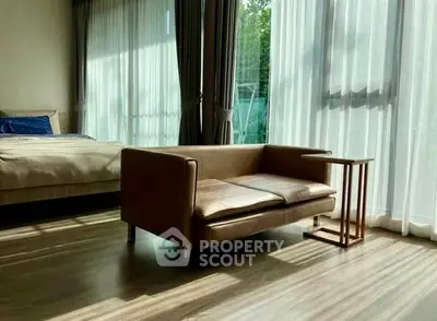 Spacious bedroom with modern sofa and large windows offering natural light