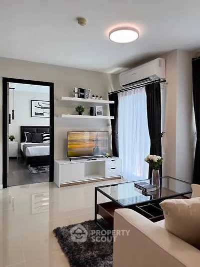 Modern living room with sleek furniture and large window, leading to a stylish bedroom.