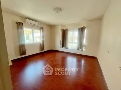Spacious empty room with wooden flooring and large windows for natural light.