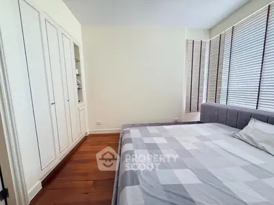 Spacious bedroom with large windows and wooden flooring, featuring a comfortable bed and built-in wardrobe.