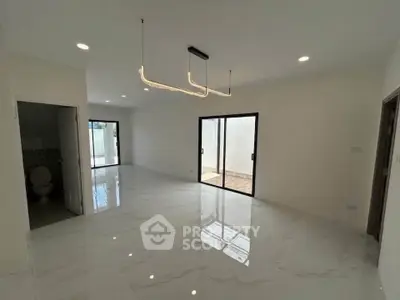 Spacious modern living room with sleek lighting and large sliding doors opening to a bright outdoor area.