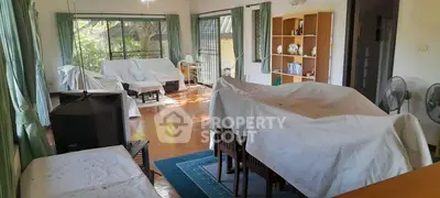 Spacious living room with covered furniture and large windows for natural light.