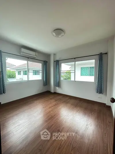 Spacious empty bedroom with wooden flooring and large windows in a modern home.