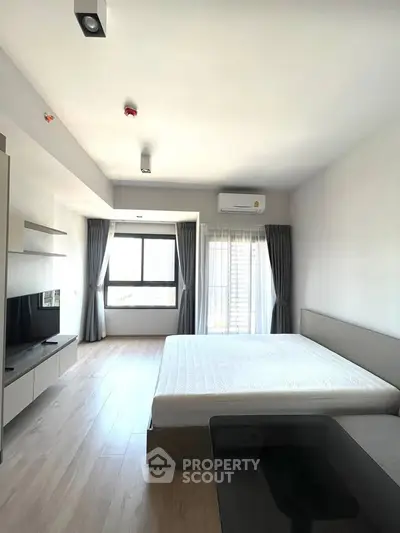 Spacious modern bedroom with large windows and natural light, featuring minimalist design and sleek furnishings.