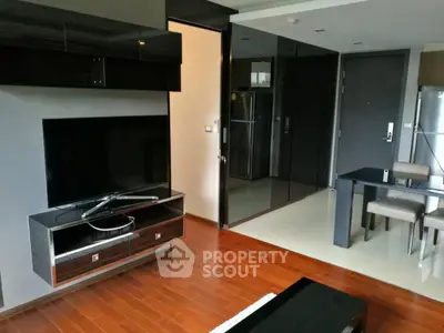 Modern living room with sleek black furniture and wooden flooring, featuring a flat-screen TV and dining area.