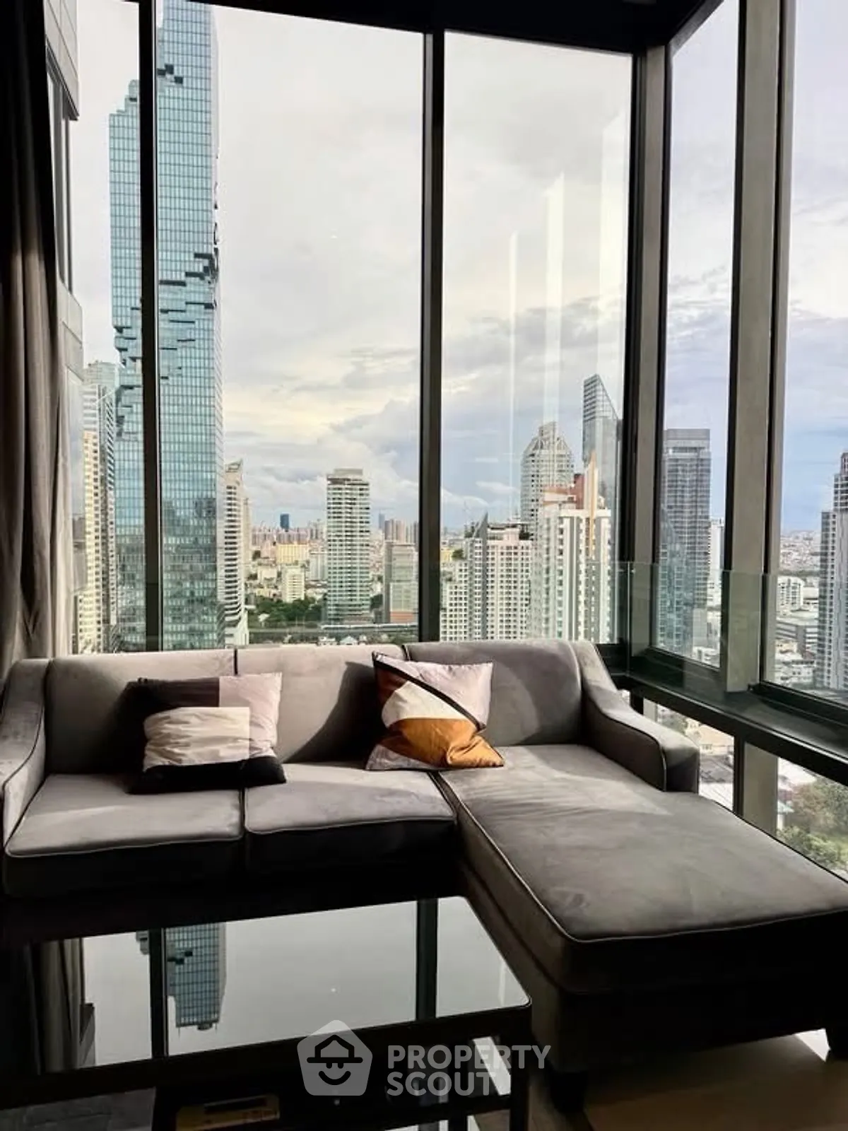 Luxurious living room with panoramic city view from high-rise apartment, featuring modern sofa and floor-to-ceiling windows.