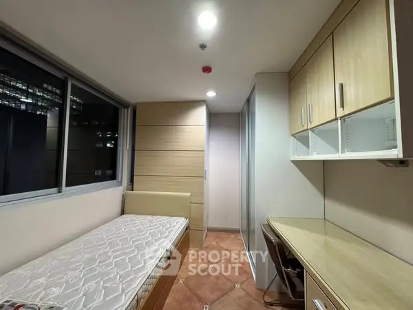 Compact bedroom with single bed, built-in wardrobe, and study desk in modern apartment.