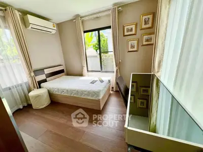 Cozy bedroom with wooden flooring, large windows, and modern decor in a bright, airy space.