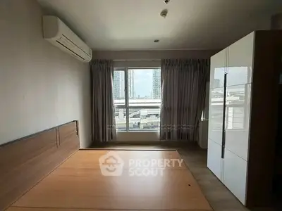 Spacious bedroom with large window offering city views, featuring modern wardrobe and air conditioning.