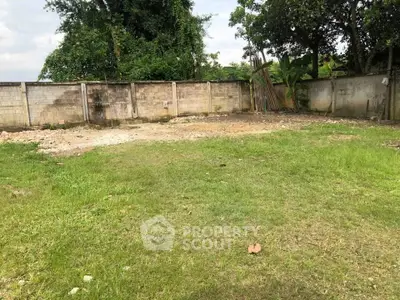 Spacious vacant land with lush greenery and privacy wall, ideal for development.