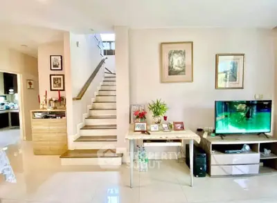 Spacious living room with modern decor and staircase, featuring a TV and elegant furniture.