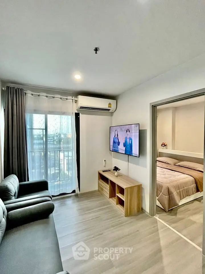 Modern living room with sleek furniture and wall-mounted TV, adjacent to a cozy bedroom with natural light.