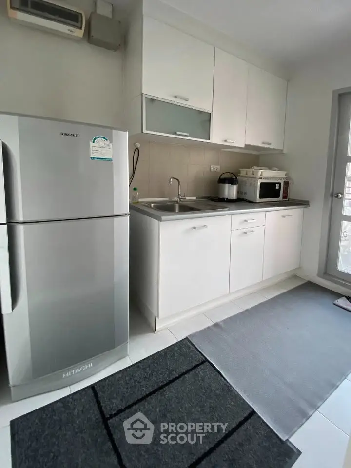 Modern kitchen with sleek white cabinets, stainless steel fridge, and microwave, perfect for culinary enthusiasts.
