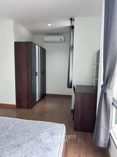 Modern bedroom with wooden flooring, wardrobe, and natural light from large window.