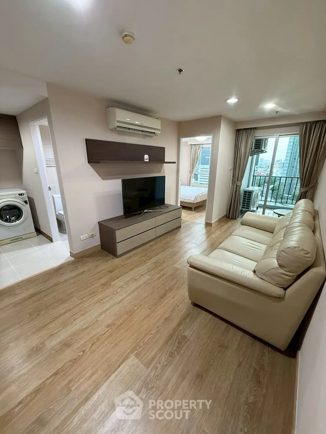 Modern living room with wooden flooring, beige sofa, and wall-mounted TV in a cozy apartment.