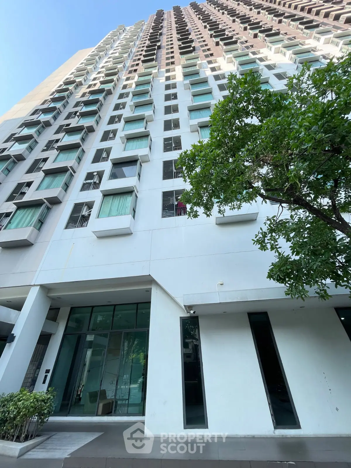 Modern high-rise building exterior with glass entrance and lush greenery.