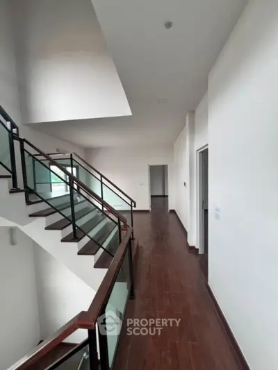 Spacious modern hallway with sleek wooden flooring and glass railing staircase