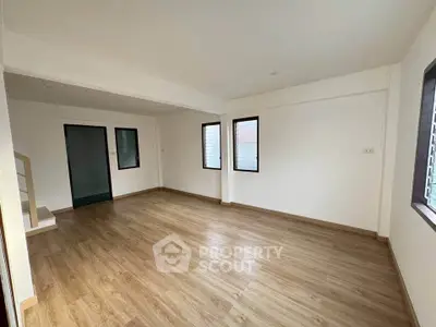 Spacious empty room with wooden flooring and large windows in modern apartment.