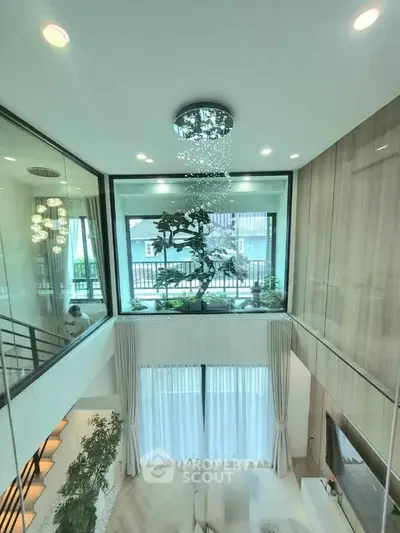 Luxurious modern living room with high ceiling and elegant chandelier, featuring large windows and stylish decor.