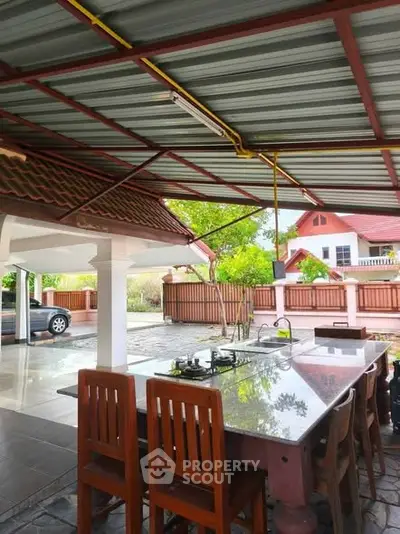Charming outdoor kitchen with gas stove and dining area in a serene residential setting.