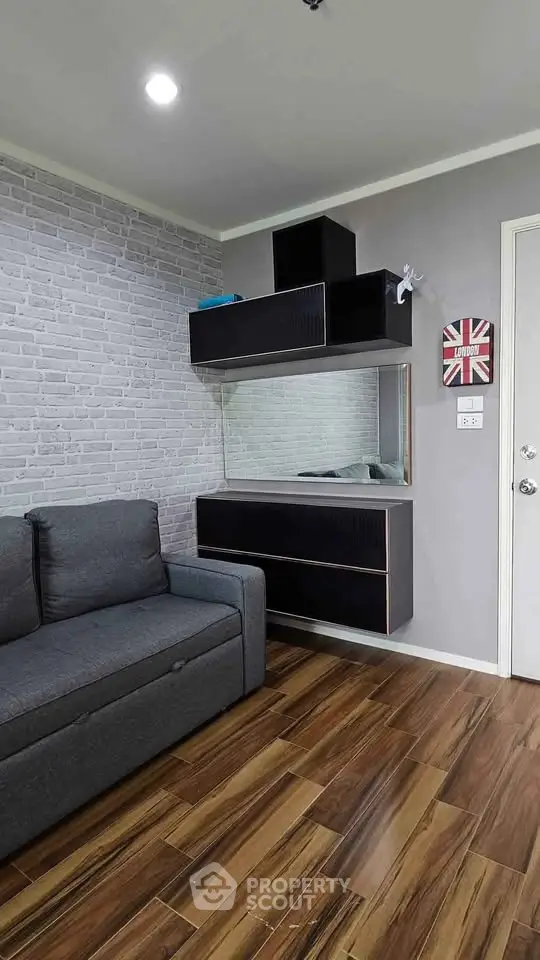 Modern living room with stylish gray sofa, wood flooring, and sleek black shelving unit.