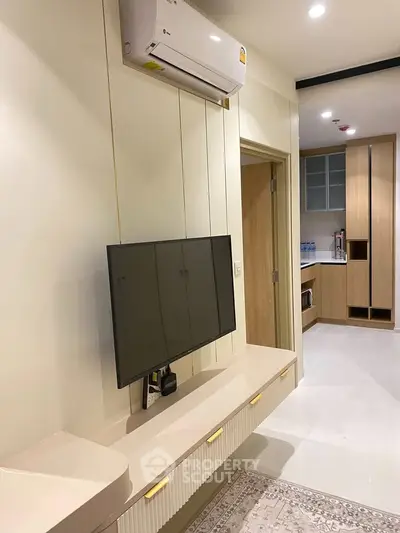 Modern living room with wall-mounted TV and sleek kitchen area in a stylish apartment.
