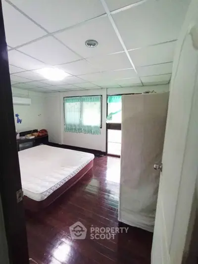Spacious bedroom with wooden flooring and natural light, featuring a comfortable mattress and ample storage space.
