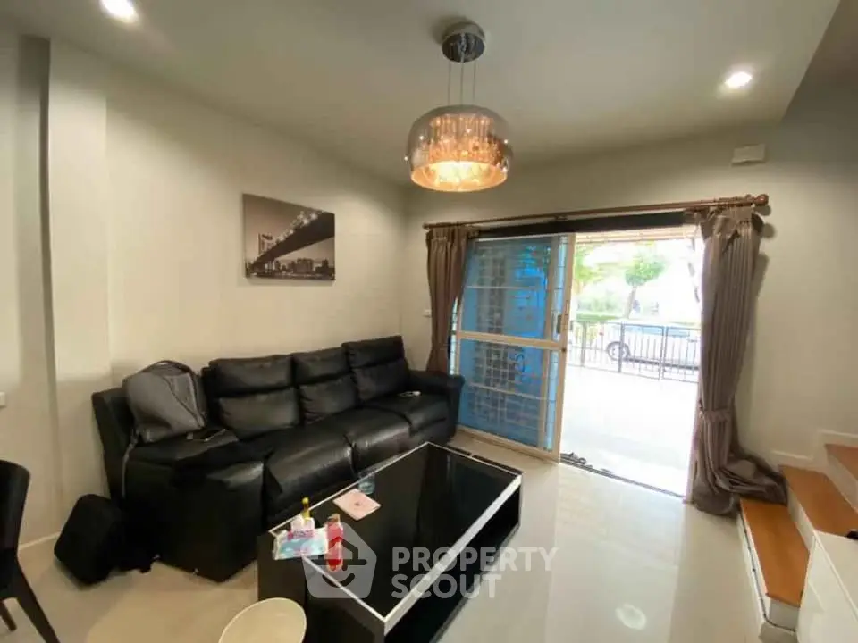 Modern living room with black leather sofa and glass coffee table, featuring elegant lighting.