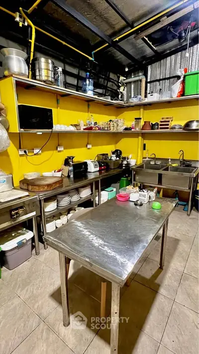 Spacious commercial kitchen with stainless steel counters and vibrant yellow shelving.