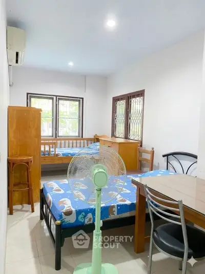 Cozy bedroom with twin beds, dining table, and fan, perfect for small living spaces.