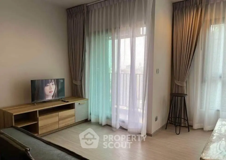 Modern living room with TV and balcony access, featuring elegant curtains and wooden flooring.