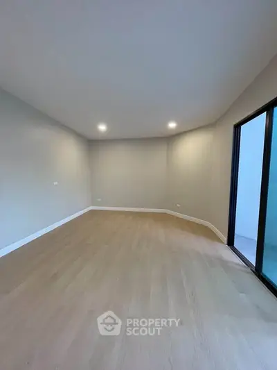 Spacious empty room with wooden flooring and large window, perfect for customization.
