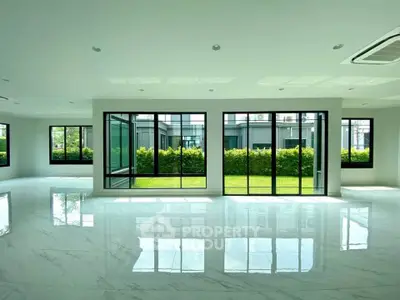 Spacious modern living room with large windows and garden view, featuring sleek marble flooring.