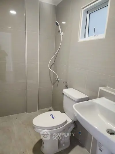 Modern bathroom with sleek fixtures and neutral tiles, featuring a shower, toilet, and sink.