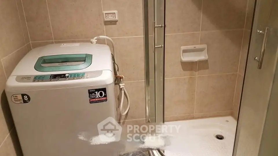 Compact bathroom with washing machine and shower enclosure in modern apartment.