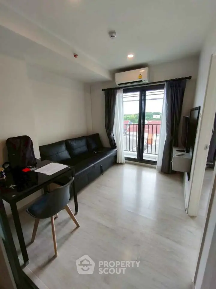 Modern living room with sleek black sofa, large window, and air conditioning unit.