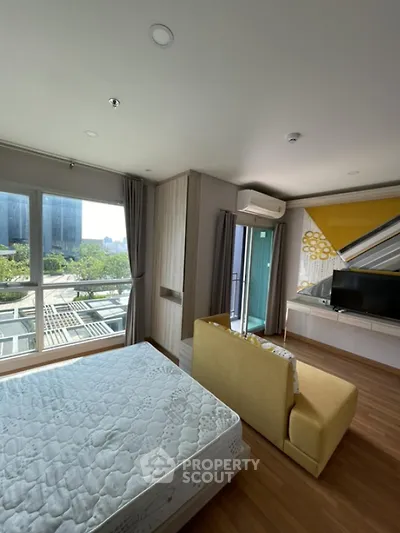 Modern bedroom with large windows and city view, featuring a cozy seating area and stylish decor.