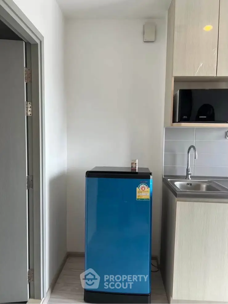 Compact kitchen with blue fridge and modern cabinetry in a cozy apartment.
