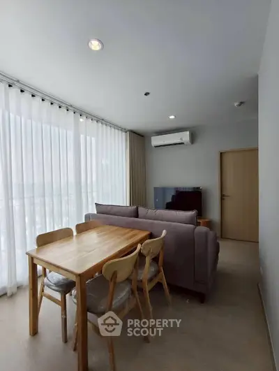 Modern living room with dining area, featuring large windows and stylish furniture.