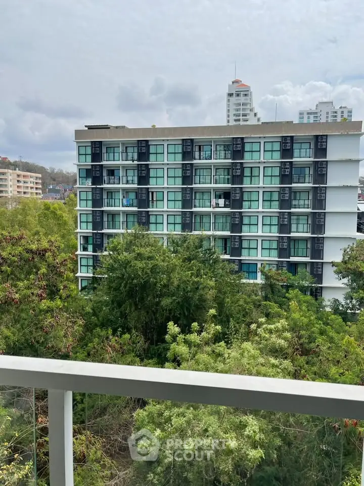 Modern apartment building with lush greenery and city view from balcony.