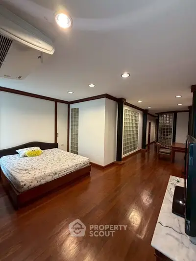 Spacious bedroom with wooden flooring and modern lighting in a stylish apartment.