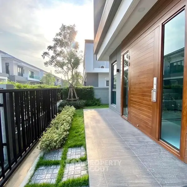 Modern townhouse entrance with sleek wooden door and lush garden view.