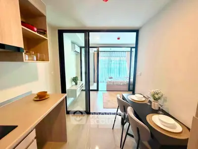 Modern open-layout kitchen and dining area leading to a cozy bedroom with glass partition.