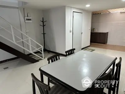 Spacious dining area with modern table and chairs, adjacent to a sleek staircase and minimalist kitchen.