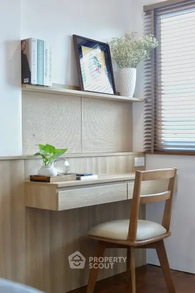 Cozy study nook with wooden desk, chair, and natural light from window blinds.