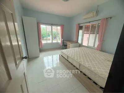 Spacious bedroom with large windows and natural light, featuring a comfortable bed and air conditioning.