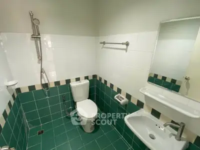 Modern bathroom with green tiles and white fixtures, featuring a shower and toilet.