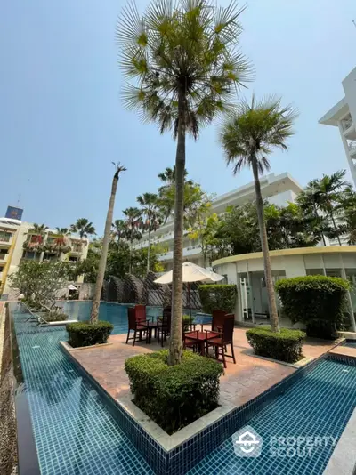 Luxurious outdoor pool area with palm trees and seating in a modern residential complex.